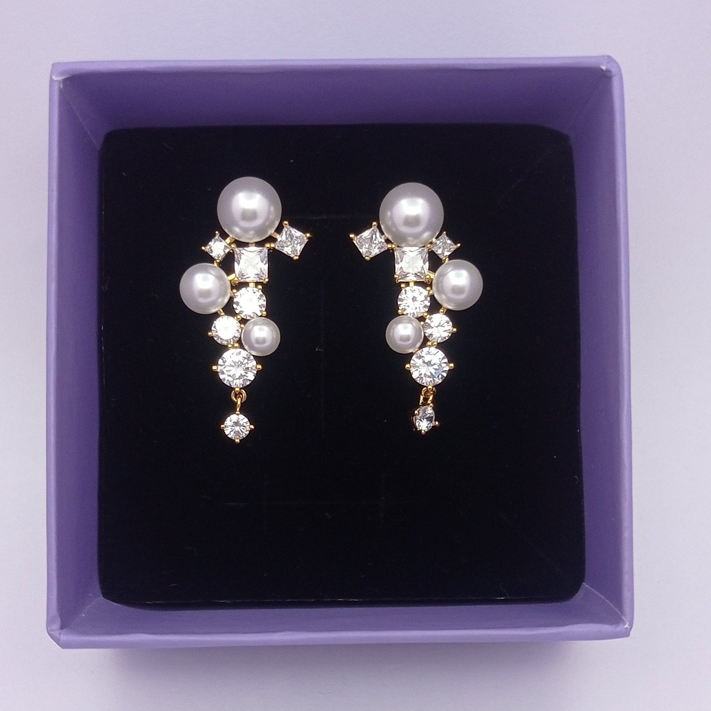 Pair of pearl earrings in a purple box on a light purple background
